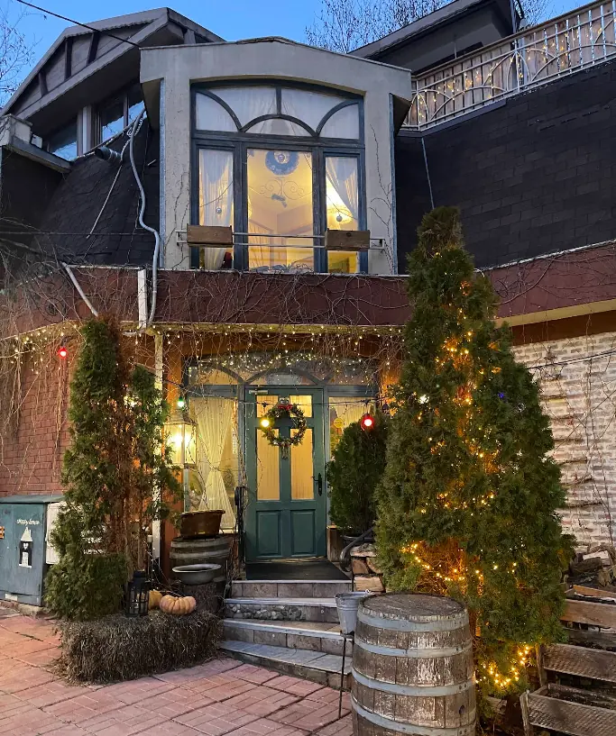 Фасадата на Bistro Happy House със зелена врата и коледни светлини